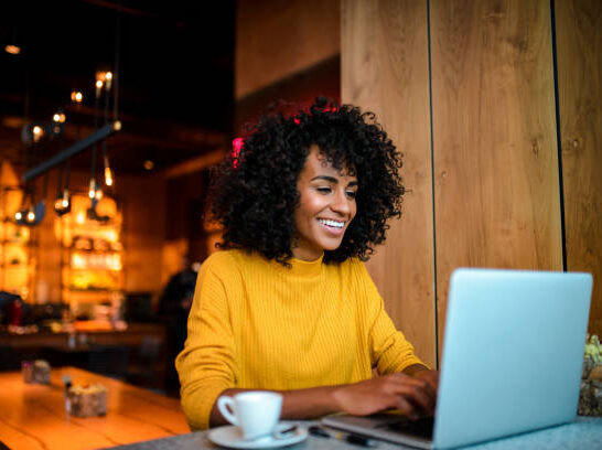 Beautiful smiling African American woman using laptop at the bar.