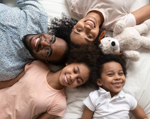 Top view portrait of happy young african American family with boy and girl kids lying on bed relaxing, smiling black parents rest with little daughter and son look at camera posing in home bedroom